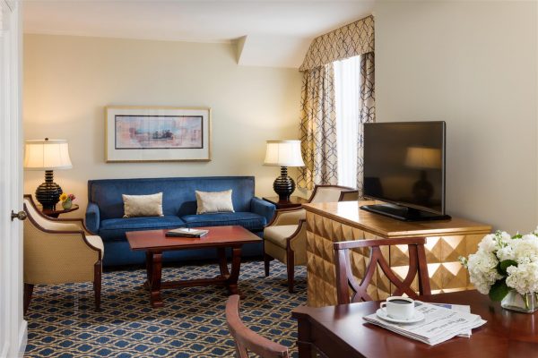 Our Francis Marion Suite features a blue sofa two gold chairs in the living room space. To the right hand side is a small dining table with a few chairs. The space features blue and gold accents throughout.