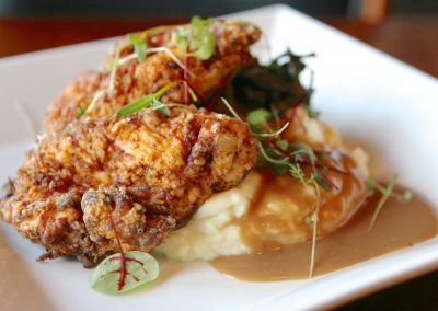A close up of a piece of fried chicken sit on top of mashed potatoes with a brown gravy.