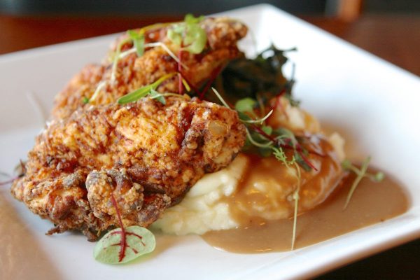 A close up of a piece of fried chicken sit on top of mashed potatoes with a brown gravy.