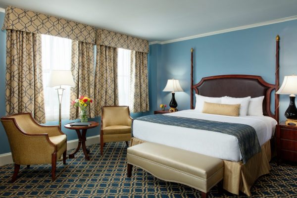 Our deluxe room features bright blue and gold features with a comfortable queen size bed. Two gold chairs are to the side.
