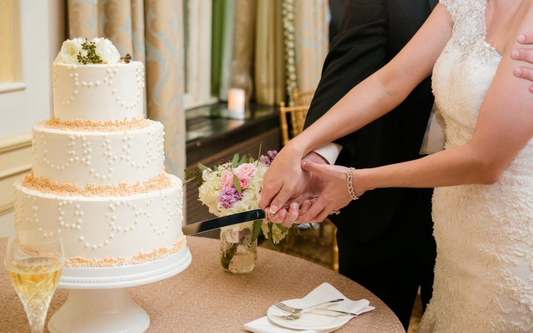 A bride and groom cut a white wedding cake together.