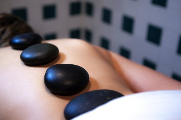 Four black stones rest on the back of a person's spine.
