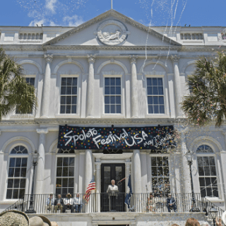 A large white historic building with a black banner that reads spoleto festival USA.