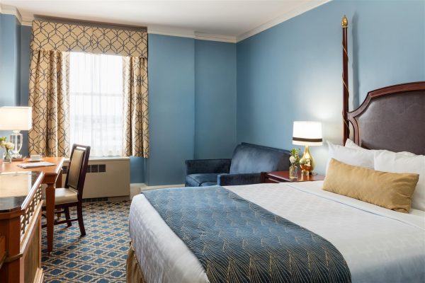 Traditional bedroom with blue walls and yellow accents. A blue sofa couch and a desk are also in the room.