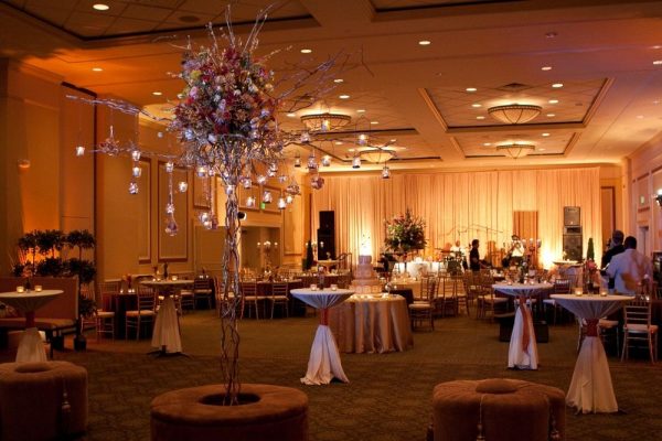 Our Carolina Ballroom is decorated for a wedding. An ornate floral display with candles hanging is int he center. Dark brows and pinks are throughout the ballroom.
