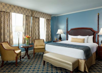 Our deluxe room features bright blue and gold features with a comfortable queen size bed. Two gold chairs are to the side.