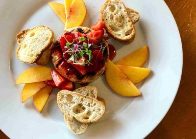 A round white plate sits that has peaches and crostini's around a piece of brie with strawberries on top.