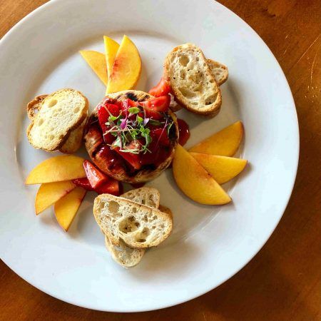A round white plate sits that has peaches and crostini's around a piece of brie with strawberries on top.