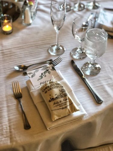 A close up of a place setting includes a personalized bag of grits and a menu.