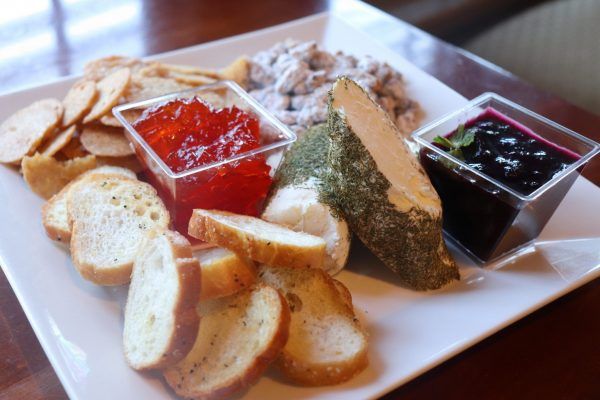 A square plate with crostinis, two different jams and a cheese in the middle.