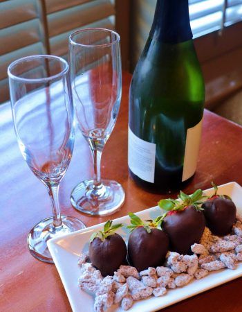 Four chocolate covered strawberries and a bottle of wine and tow glasses.