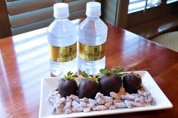 Four chocolate covered strawberries sit on a small rectangular plate. Two small water bottles sit behind the plate.