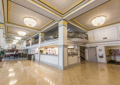 The front desk of the hotel sits in the lobby area with blue and gold features and large chandeliers on the ceiling.