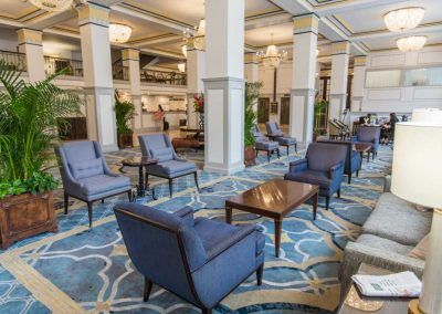 A sitting area of the hotel lobby features multiple blue chairs and views of the elegant blue and gold accents throughout the space.