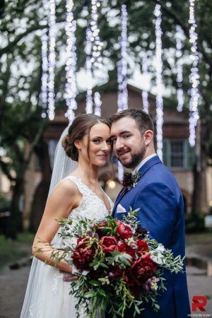 A bride and groom stand cheek to cheek and the bride holds a bouquet of flowers.