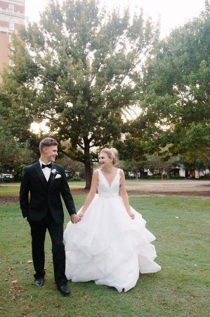 A bride and groom walk holding hands and laughing with each other in a park.
