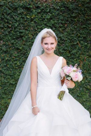 A bride smiles at the camera and holds her bouquet.