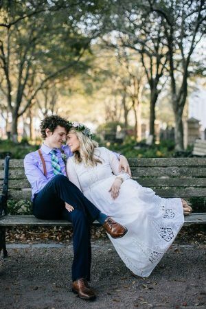 A bride and groom sit with each other and cuddle on a park bench,