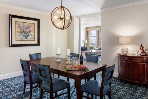 A dining room area is set with two large candles and a plate of meats and cheeses. A large exposed lightbulb fixture hangs above the table.