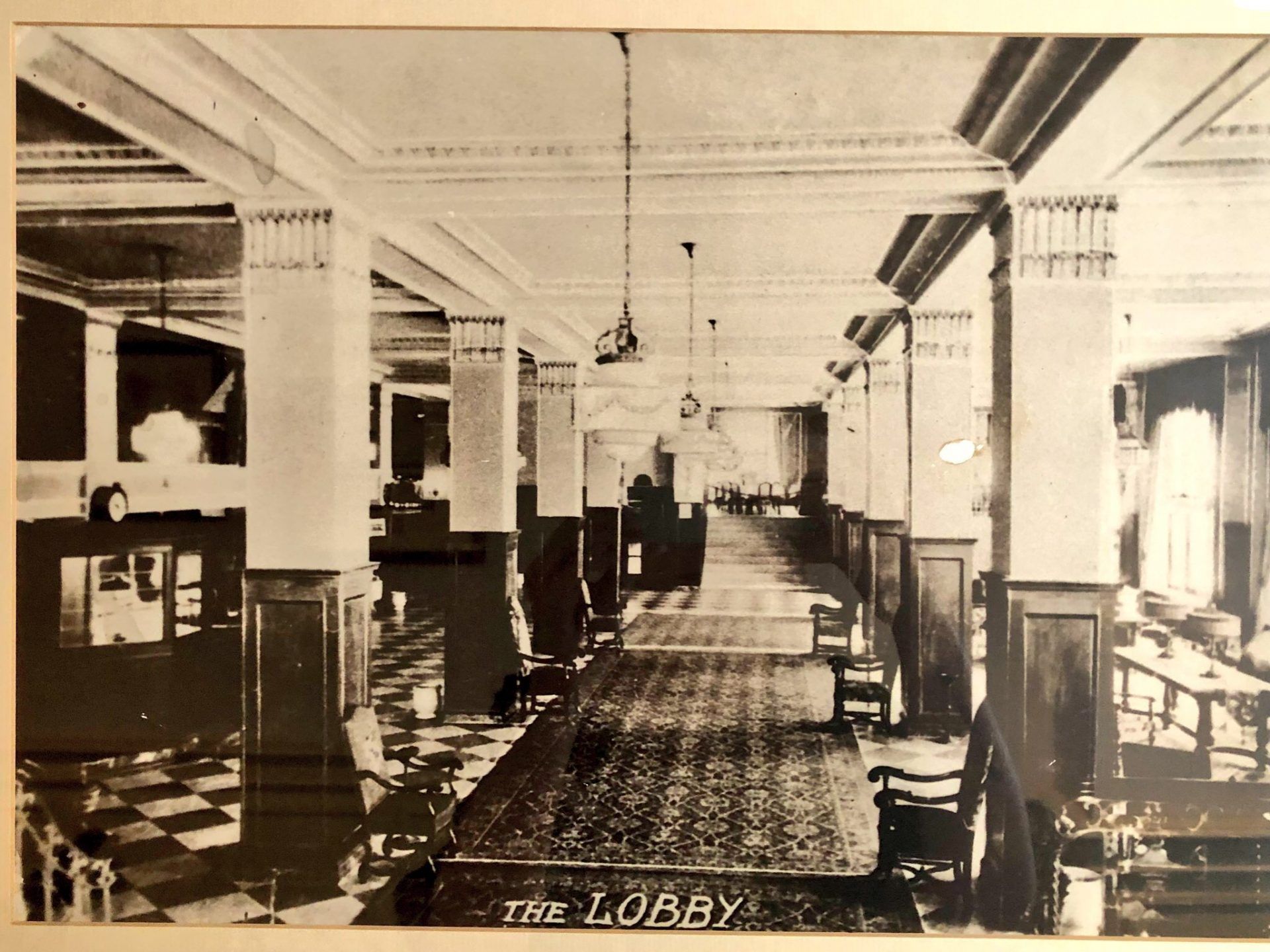 A photo of the original lobby is in sepia and shows square tile flooring and carpeted middle walk ways.