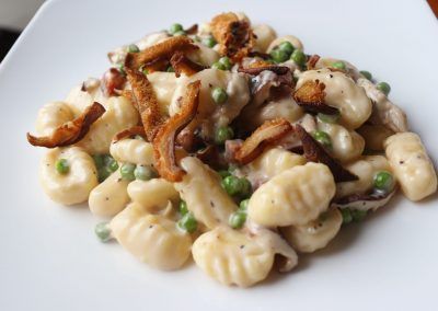 A close up of white creamy gnocchi with green peas and small slices of bacon.