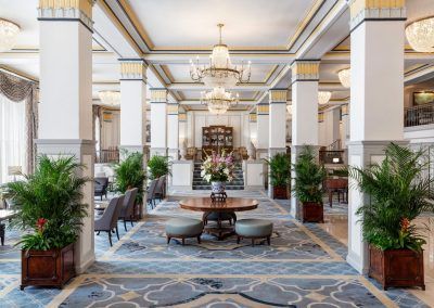 The lobby of the hotel showcases plenty of natural light with blue and gold carpet. A beautiful flower display sits in the center of the room on a round table.