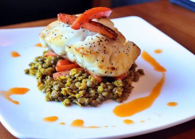 A square plate has a mash of green peas and carrots with a white piece of fish on top.