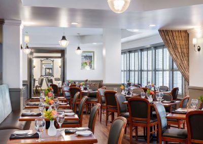 A dining room with wood floors and light grey walls. Chairs and tables fill the space.