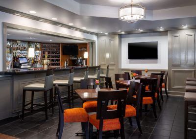 The bar area of the swamp fox restaurant has five bar seats and three tables with four chairs around them. A tv hangs on the wall.