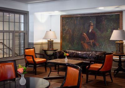 The lounge area of the restaurant shows orange chairs and a brown leather couch up against a wall with a large painting of a man on a horse.