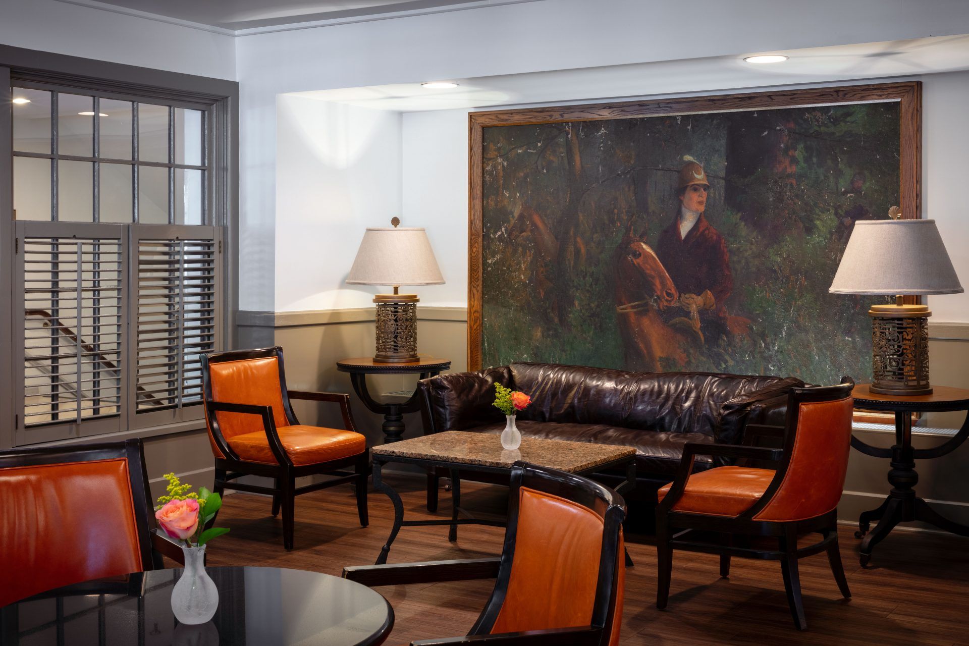 The lounge area of the restaurant shows orange chairs and a brown leather couch up against a wall with a large painting of a man on a horse.