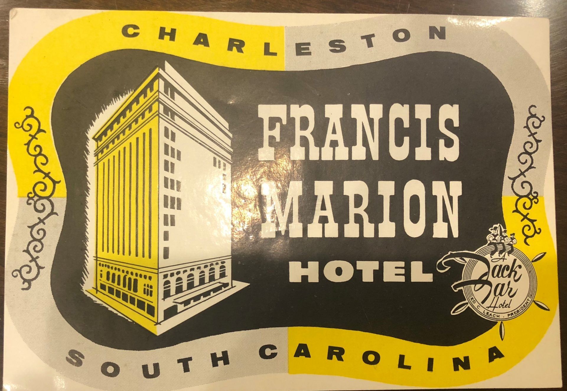 A grey and yellow postcard that reads Charleston, south Carolina. In the middle is a drawing of the exterior of the hotel and says Francis Marion Hotel.