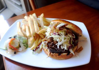 A barbeque sandwich with coleslaw with French fries sits on a white plate.