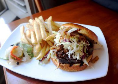 A barbeque sandwich with fries sits on a white plate.