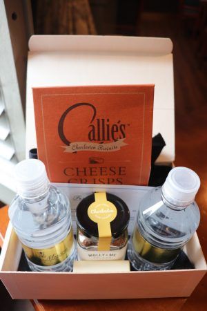 A box is opened and two water bottles with a small jar and a bag that says cheese crisps sits inside.