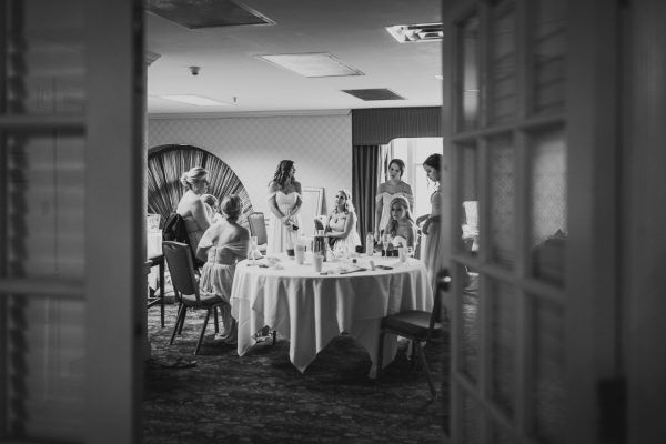 A black and white image of a bridal party sitting around a table getting ready.