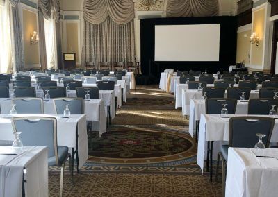 A ballroom space with large chandeliers and rows of long tables and chairs.