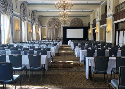 A ballroom space with large chandeliers and rows of long tables and chairs.