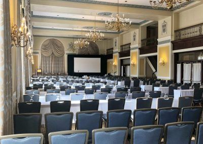 A ballroom space with large chandeliers and rows of long tables and chairs.