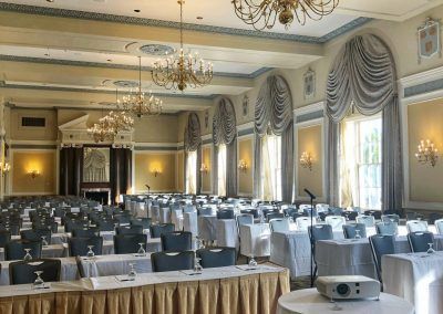 A ballroom space with large chandeliers and rows of long tables and chairs.