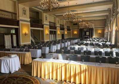 A ballroom space with large chandeliers and rows of long tables and chairs.