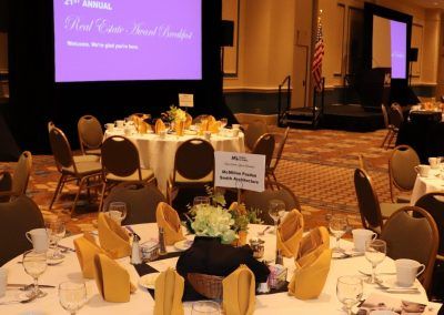 A ballroom with two large screens and multiple round tables set for a conference.