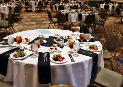 A ballroom with multiple round tables are set with salad, dessert and drinks.