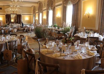 A ballroom space is set with multiple large tables that are set with extravagant floral displays in the middle that include large feathers.