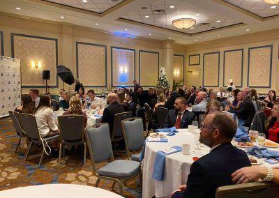 Multiple tables with people sitting around them inside a ballroom space.