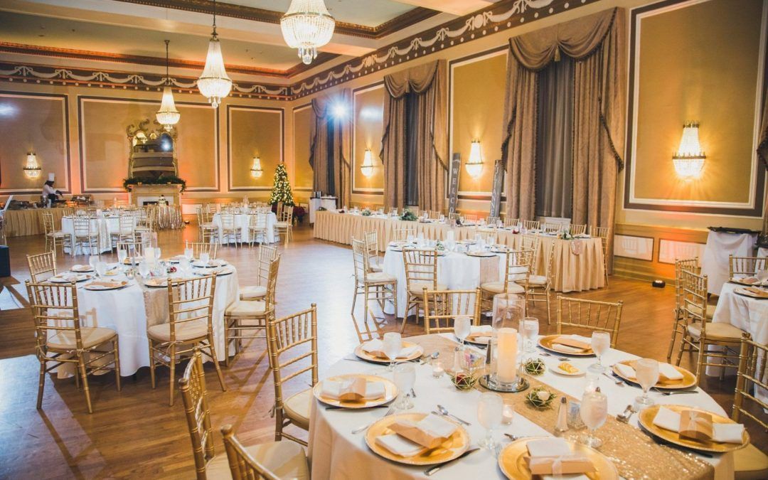 A ballroom in the hotel that is called the Gold Ballroom with wooden floors and gold chairs with antique chandeliers. A grand mirror is against the golden walls.