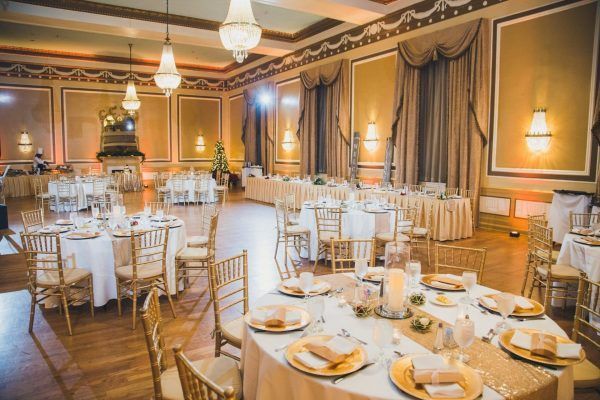 A ballroom in the hotel that is called the Gold Ballroom with wooden floors and gold chairs with antique chandeliers. A grand mirror is against the golden walls.