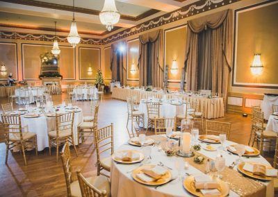 A ballroom in the hotel that is called the Gold Ballroom with wooden floors and gold chairs with antique chandeliers. A grand mirror is against the golden walls.