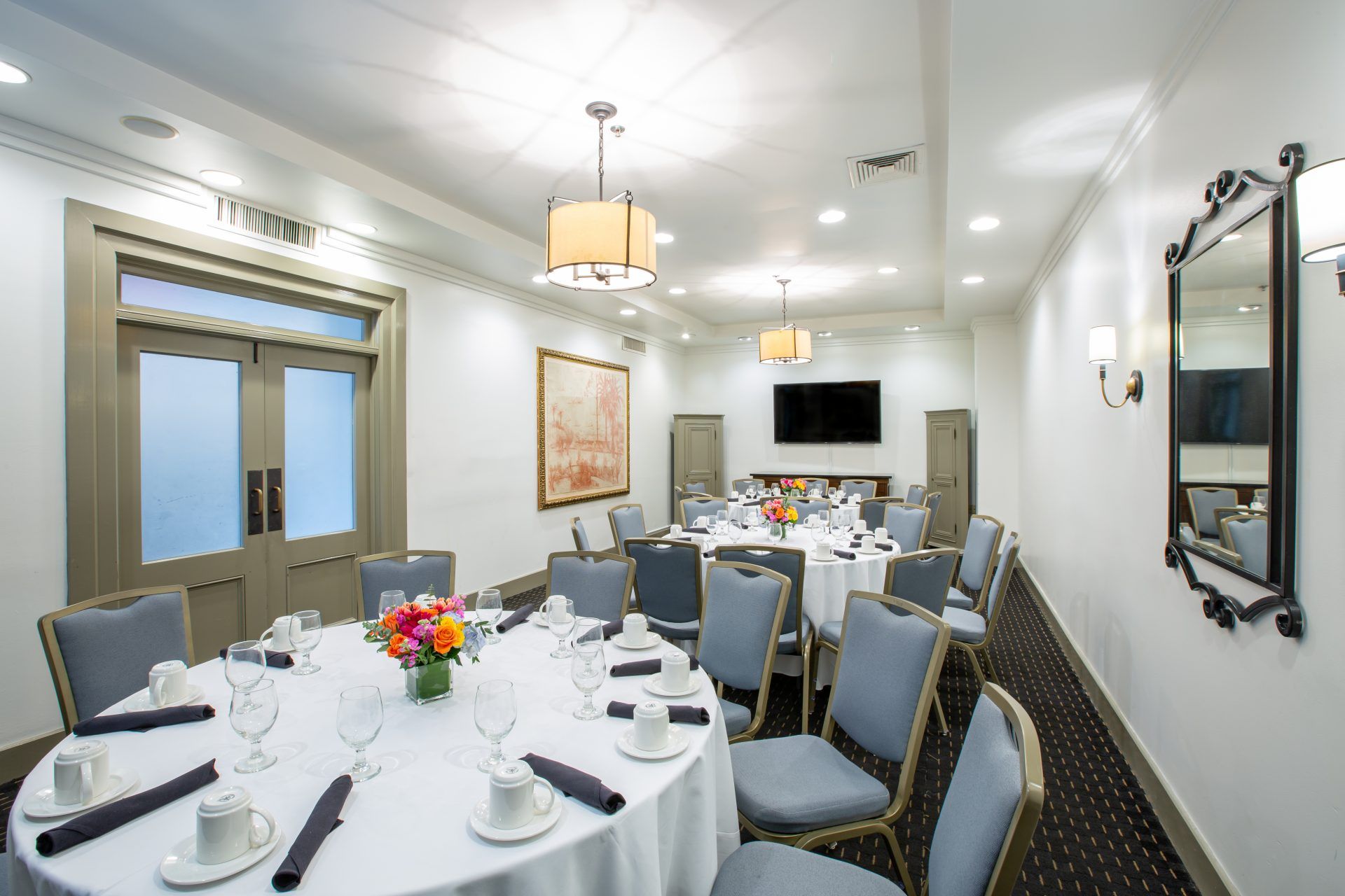 Three round tables with blue chairs around them sit in a private dining room space. The tables have brightly colored floral displays and coffee mugs sit on the tables.