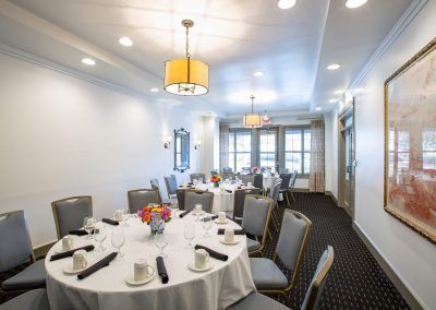 Three round tables with blue chairs around them sit in a private dining room space. THe tables have brightly colored floral displays and coffee mugs sit on the tables.